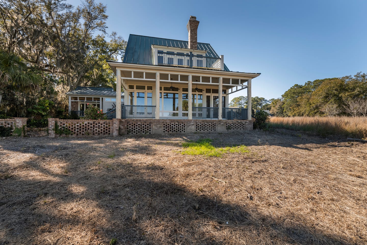The marsh-side of the original house before renovation: wraparound porch and brick lattice foundation above a bare lawn
