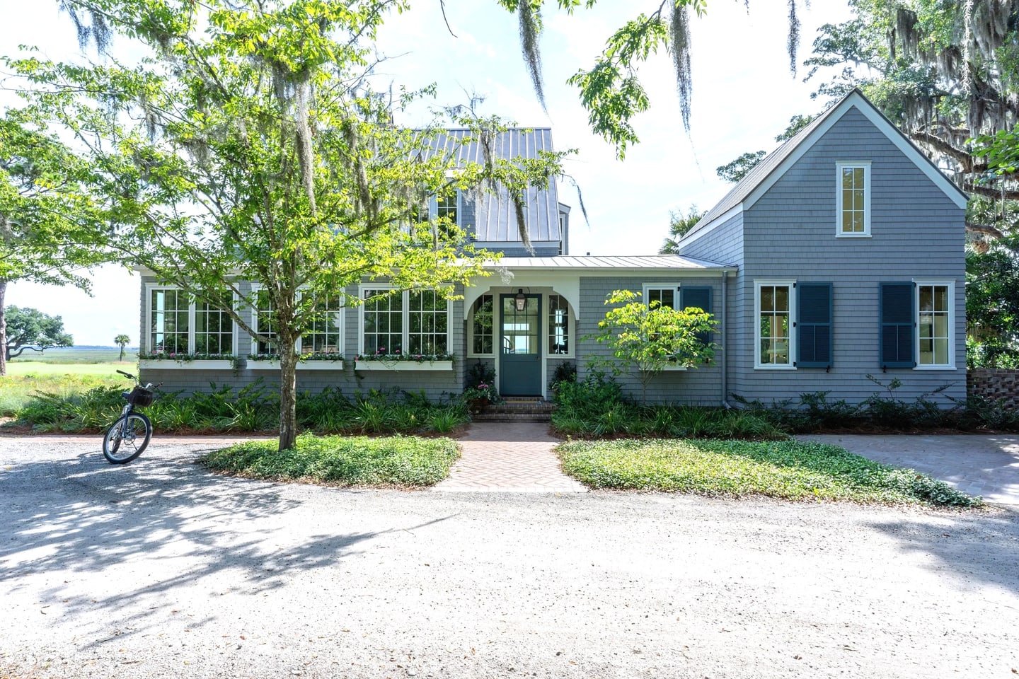 The front of the Lowcountry Waterfront Home on Spring Island: grey shingle, a green front door beneath an arched entry, and live oaks